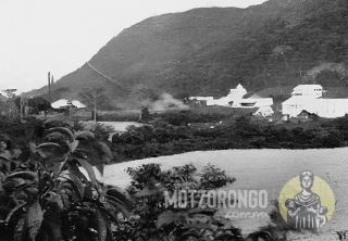Vista de la Hacienda de Motzorongo desde los terrenos que hoy ocupa el barrio Pueblo Nuevo, mostrando los edificios principales, campos con caña de azúcar recién cortada y a la distancia el pequeño ingenio con dos chimeneas.