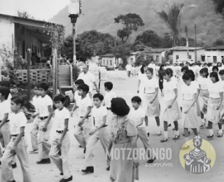 Alumnos de la Secundaria Técnica durante un desfile, marchando muy cerca de la ermita en el barrio El Nido junto a la antigua galera de casas.