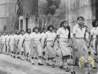 Alumnos de la Secundaria Técnica durante un desfile, marchando frente a los antiguos tanques de agua y petróleo del ingenio Central Motzorongo.