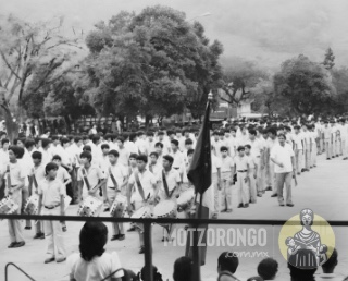 Alumnos de la Secundaria Técnica durante un desfile, llegando a la explanada del parque "Carlos A. Pacheco", fotografía tomada desde la pérgola donde se observan los antiguos árboles.