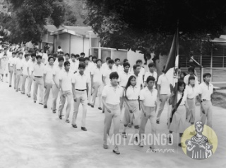 Alumnos de la Secundaria Técnica durante un desfile, llegando al parque "Carlos A. Pacheco", fotografía tomada junto a la primaria donde se observan las antiguas mallas ciclónicas donde ahora existen bardas de block.