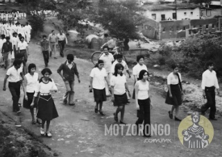 Personal de la Secundaria Técnica durante un desfile, marchando frente a la parroquia, al fondo se observan los trabajos en obra en las oficinas de Central Motzorongo.